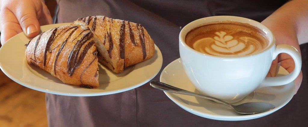 latte and chocolate croissant on two separate plates being held by server ready to enjoy