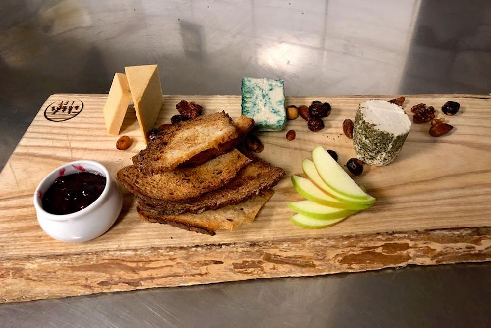 side view of charcuterie wooden board with various fruit and sauce ramekin for garnish