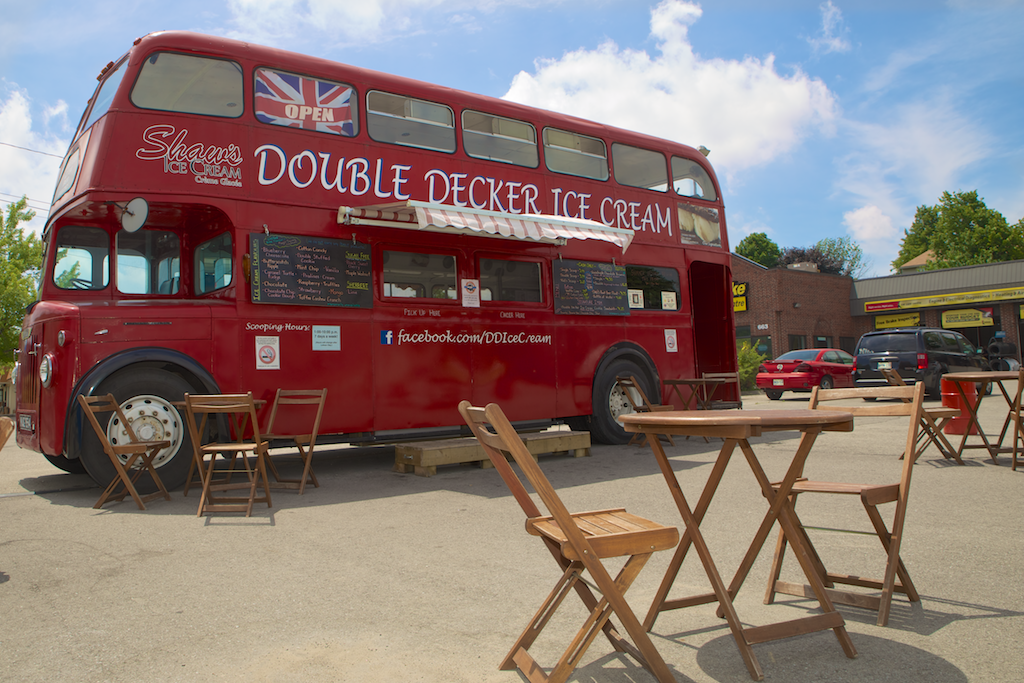 front view of red double decker bus behind patio table and chairs on road