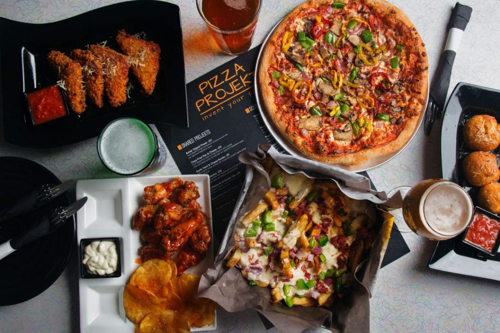 flat lay of pizza, wings, nachos and other appetizers with sauce ramekins and menu on the bottom
