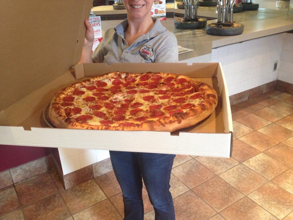 woman holding large open pizza box in front of counter