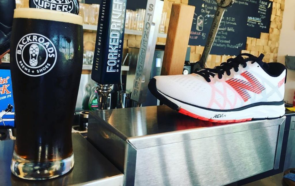 close up of white and orange running shoe beside beer taps and pint glass on a bar