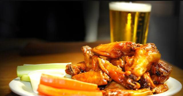 closeup of plate of wings with side carrots and pint of beer in background