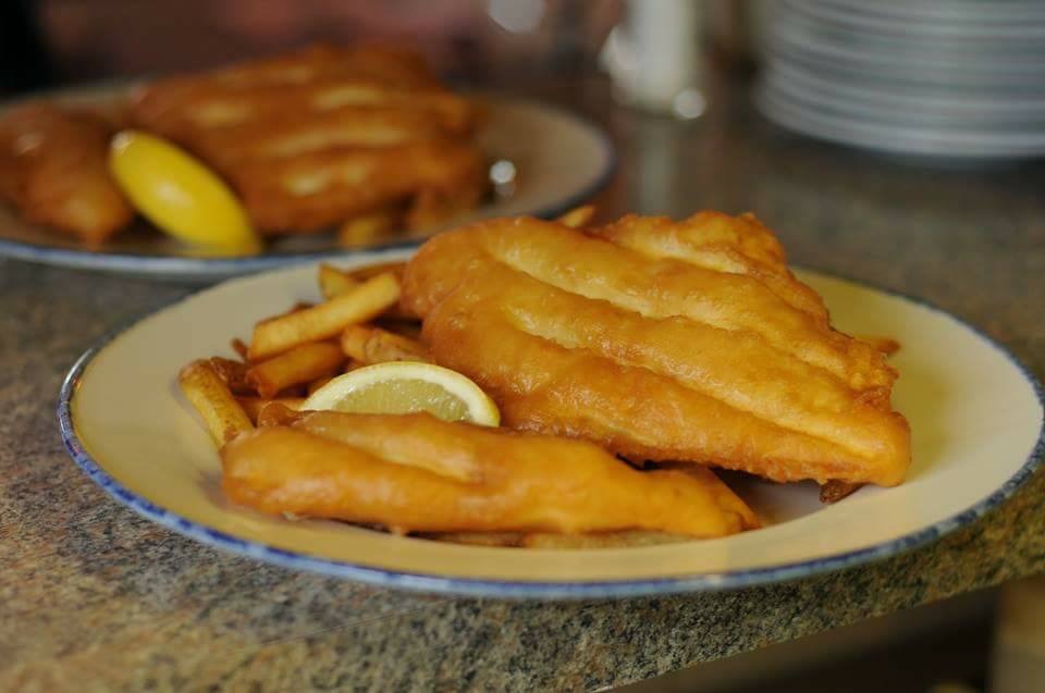 side view of two battered fish and chip plates with lemon garnish on speckle counter