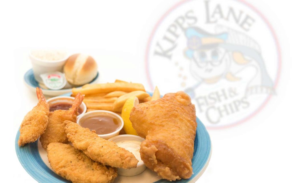 battered fish and chip plate with sauce ramekins in middle on blue plate in front of white backdrop