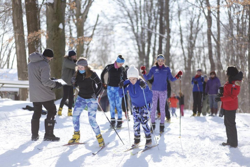 many people skiing on snow surrounding by trees many using poles moving toward camera
