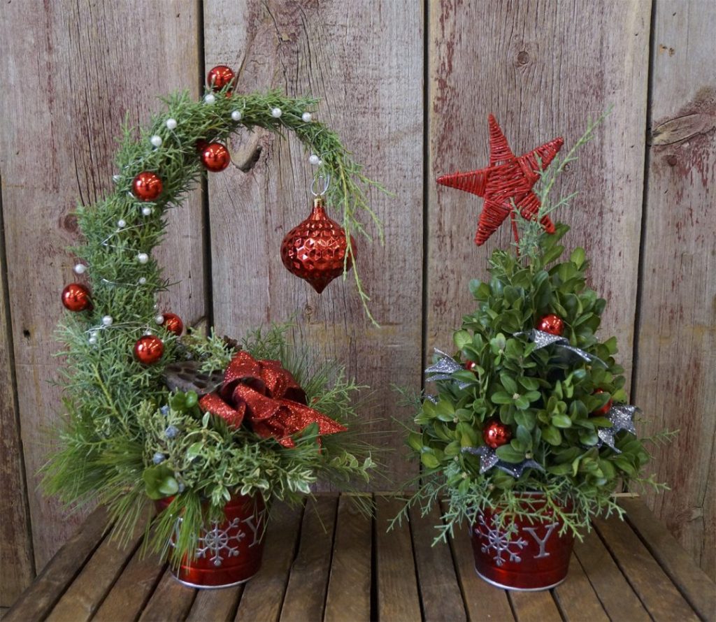 front view of two mini evergreen christmas decorations with red ornaments on both on wooden planks