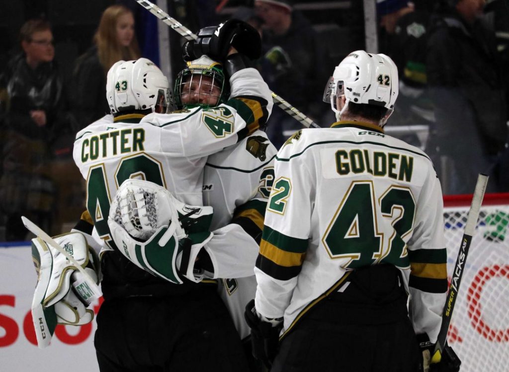 three hockey players in white jerseys gathering for a celebration with two players hugging