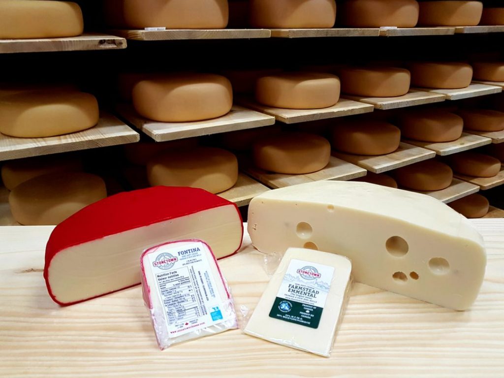 shelving units filled with cheese with two large chunks of cheese on a table in front with smaller portions wrapped to buy