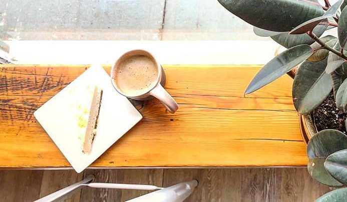 top view of wooden counter with coffee cup and piece of cake on top