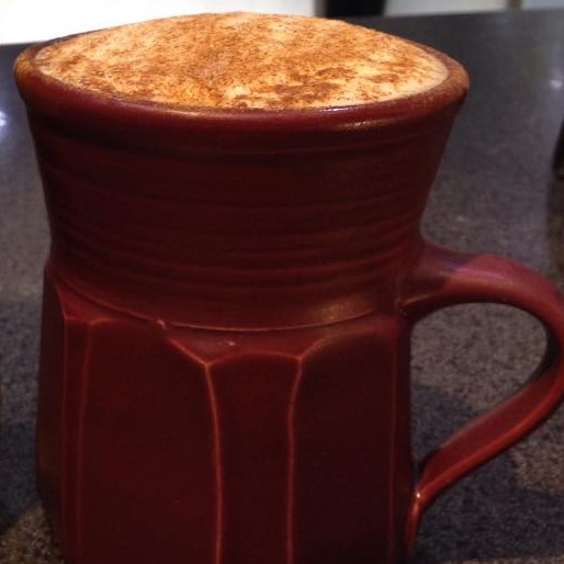 side view of red mug with brown powder on top of liquid on a dark table
