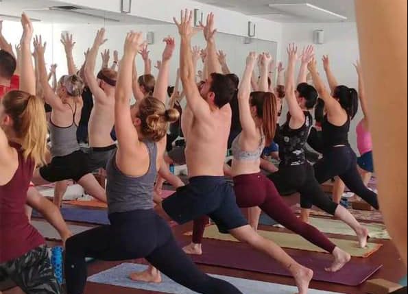 group of people doing yoga in a studio on matts with arms raised to the ceiling