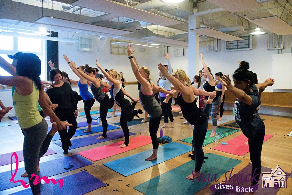 group of people doing yoga in a studio on matts with one arm holding their foot and the other in the air