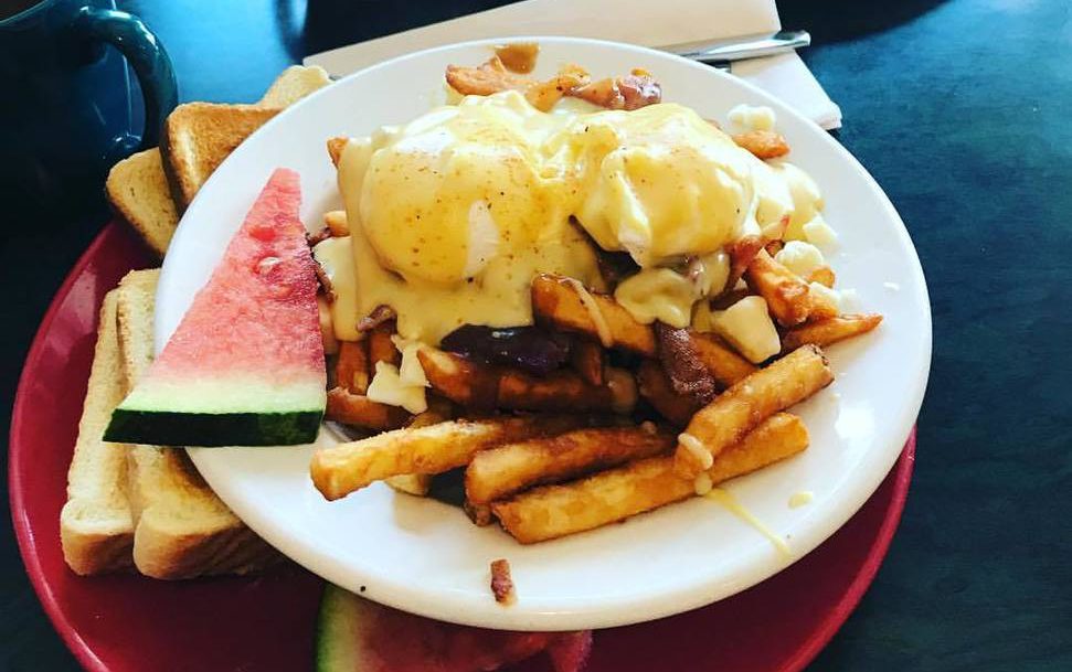 circular white plate with poutine and eggs benedict on top with a side of watermelon