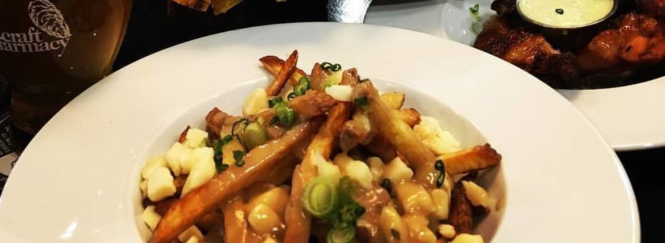 poutine in a circular white bowl with green garnish and other bowls in the background