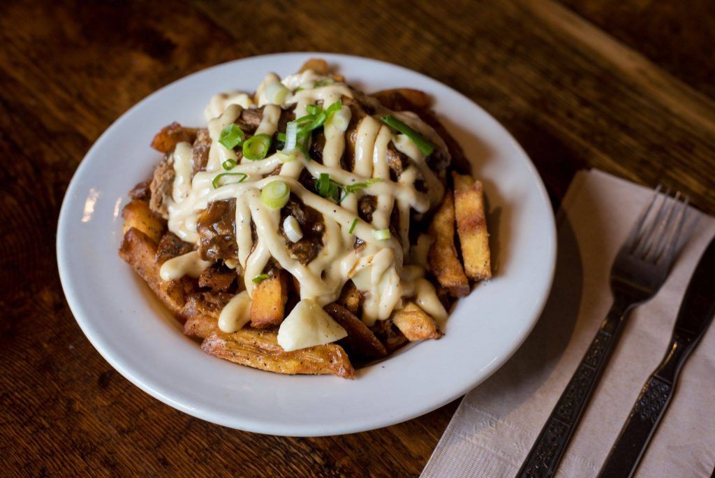 poutine in a bowl with green garnish and silverware on the side with a napkin