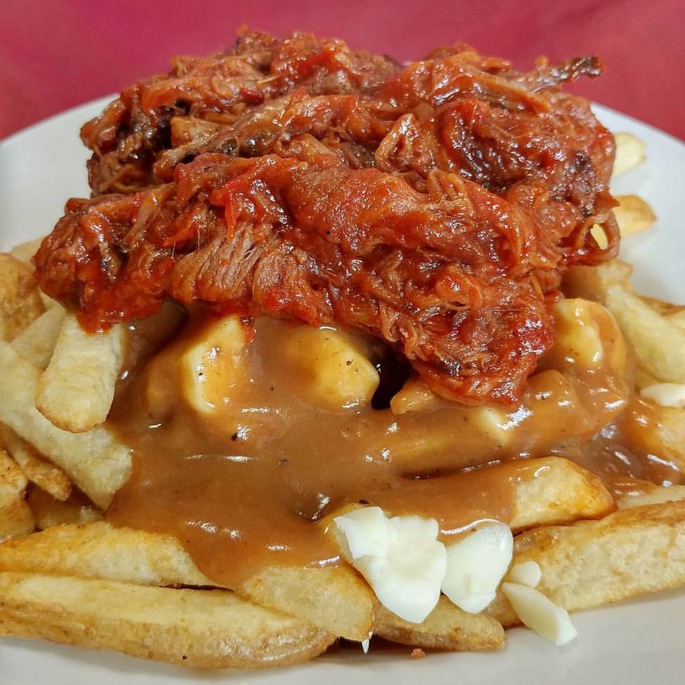 close up of poutine with pulled pork on top on a plate with a red background