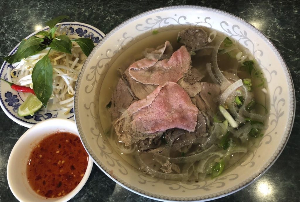 top view of pho bowl with two garnish dishes to the left