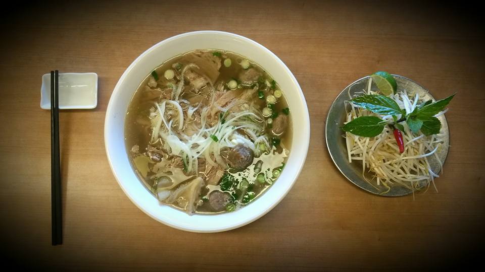 top view of pho bowl with bean sprout dish to the right and chopsticks to the left on wooden table