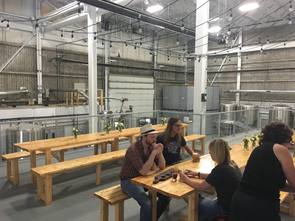 interior of second floor of brewery with vats below and picnic style tables with people sitting at them