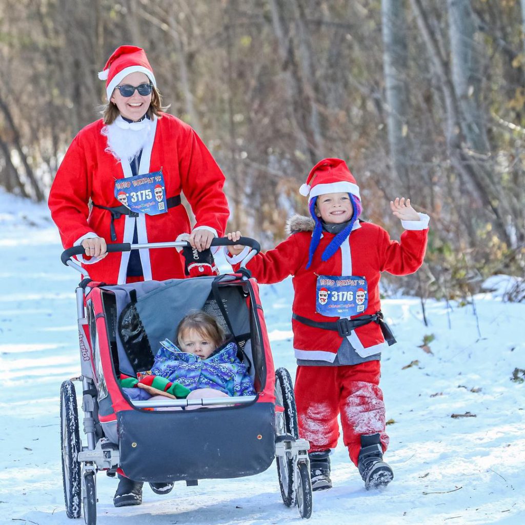 woman with stroller and child running in snow in santa costumes