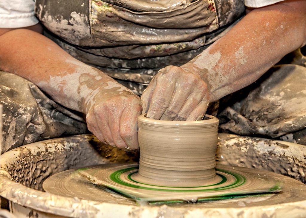 man sitting at pottery station holding loose clay forming pot