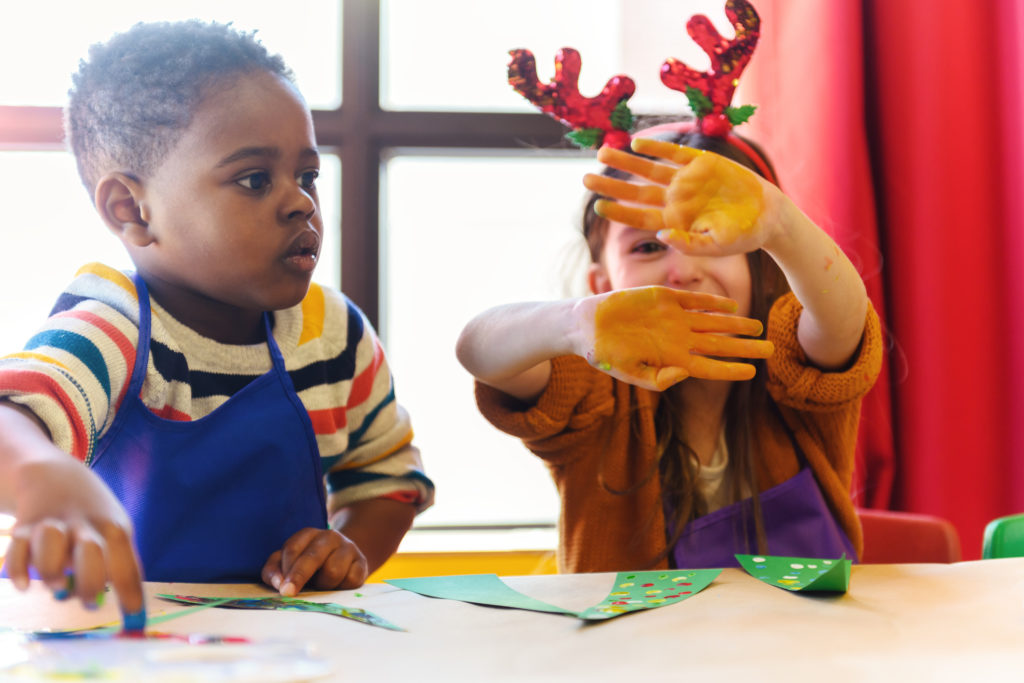 young kids doing homemade decorations for Christmas at a table with girl wearing antlers