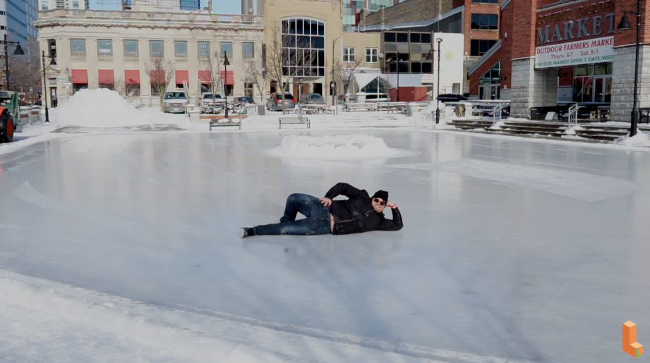 man posing lying on skating rink alone in front of some buildings