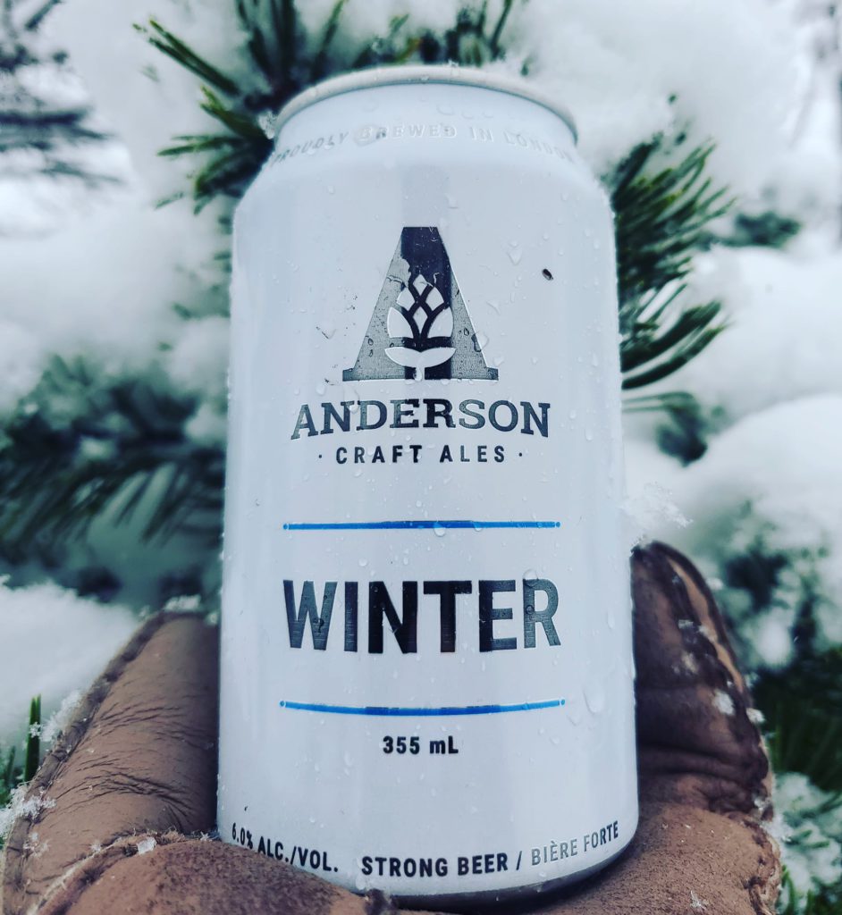 white beer can being held up infront of tree with snow