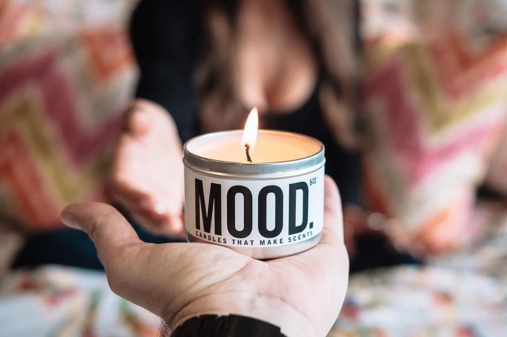 hand holding lit candle with the word mood on the front