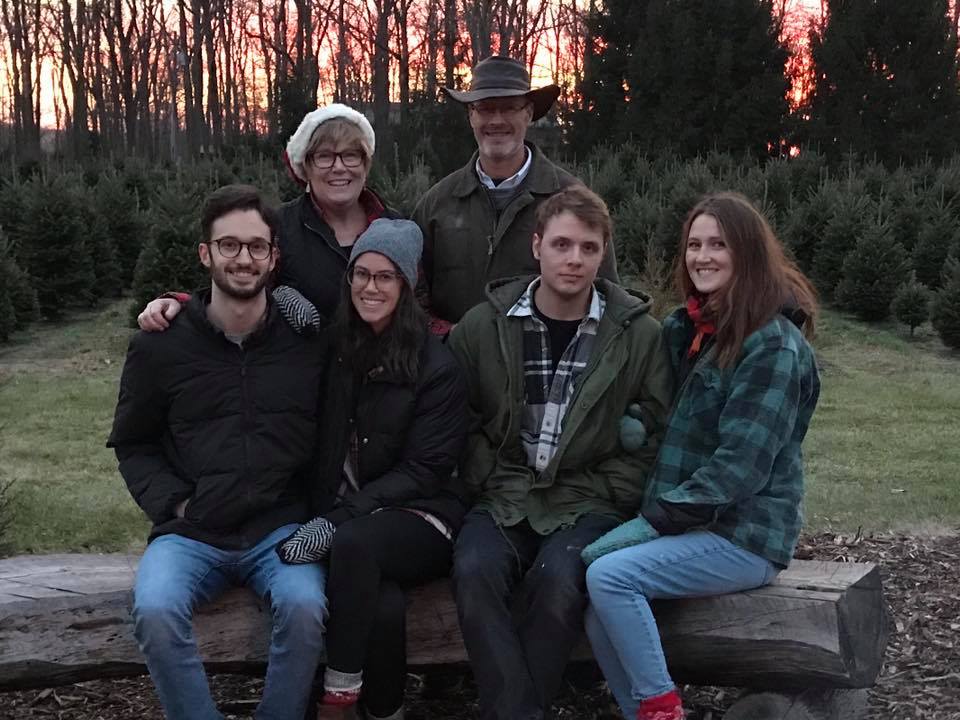 family taking posed photo sitting on tree stump during sunset all smiling at camera