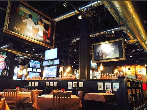 view of empty dining room in bar type restaurant with black partition in middle, many tvs and chalk decor hanging from the ceiling with short tables and booths visible