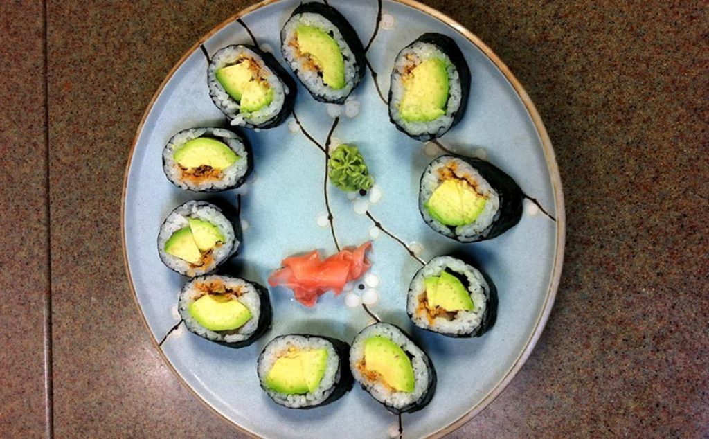 Top view of sushi plate with avocado rolls with ginger and wasabi dollops in the middle on a counter