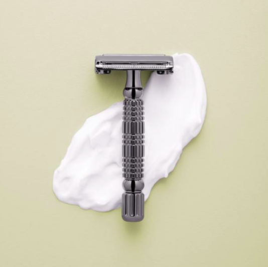 small silver razor against a green backround with shaving cream under the razor