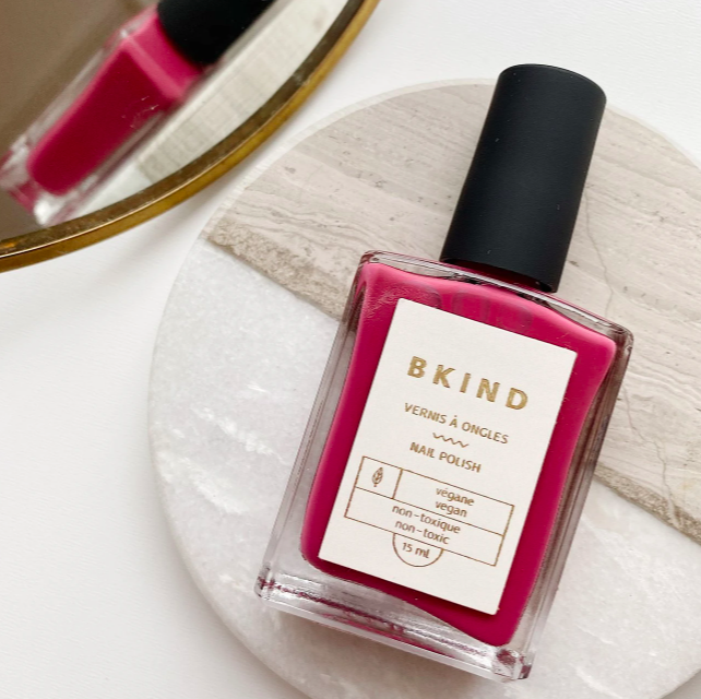 small square bottle of vegan nail polish in a magenta colour sitting on a marble type coaster beside a mirror