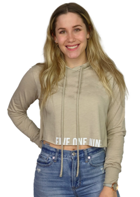 woman modelling a beige sand coloured cropped sweater with words on the bottom smiling at the camera