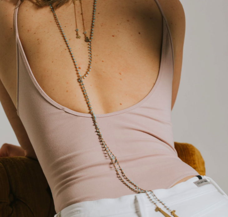 woman modelling a back dangling necklace with a pink tank top on a necklace as the focus