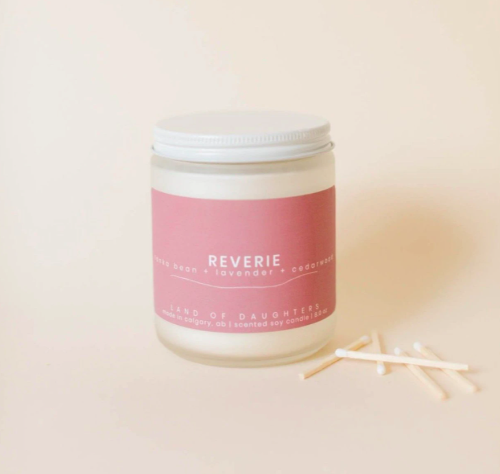 smaller organic candle with a pink wrap around the front sitting in an ivory room with some matches sitting to the side