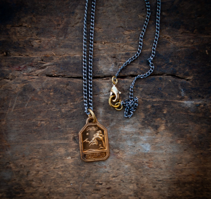 long chain necklace with gold detailing and a rectangular pendant hanging down sitting on a dark wooden table