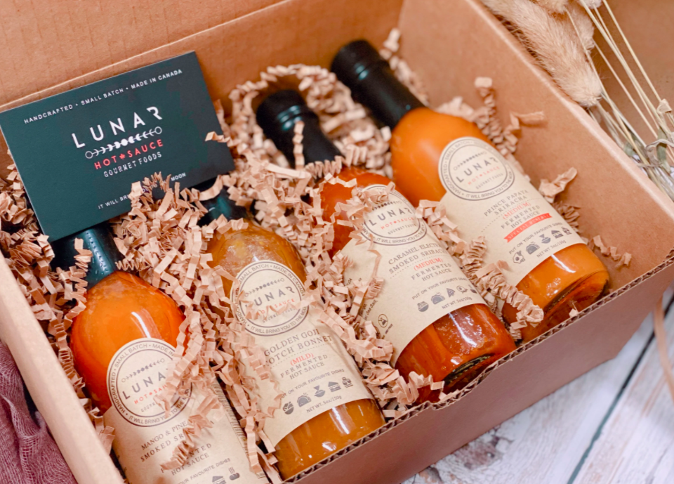 box of four hot sauce bottles with different coloured sauces inside with a black business card in the top left corner