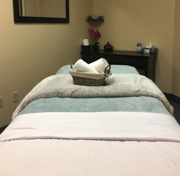 interior of a massage room with a made bed and small basket with paper towel inside