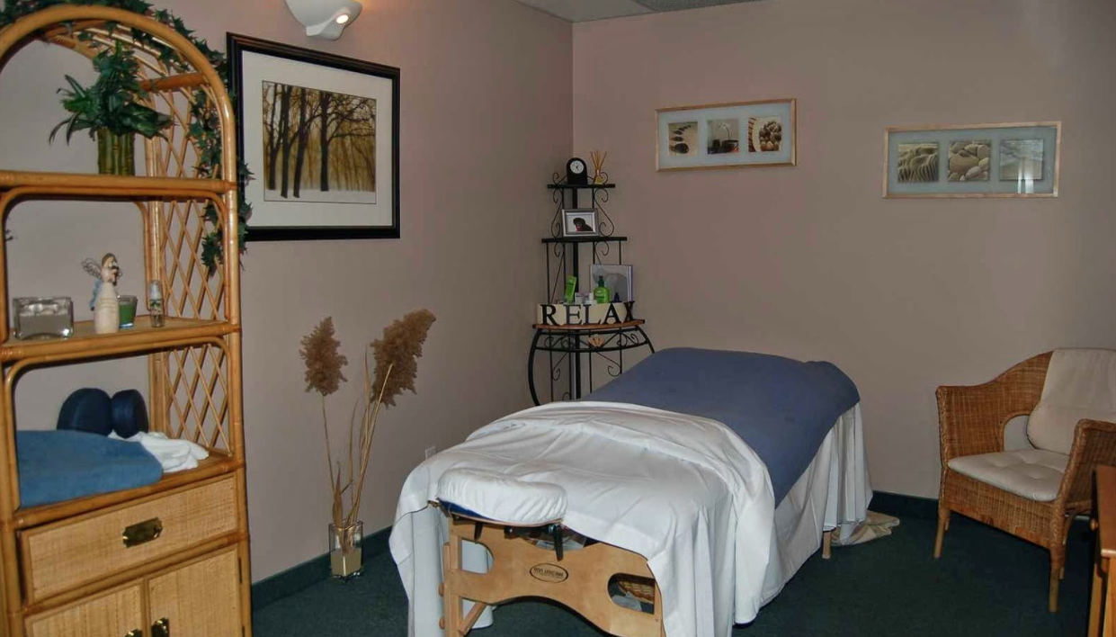 interior of a massage room with a made bed and various pieces of decor throughout the room with a chair in the corner