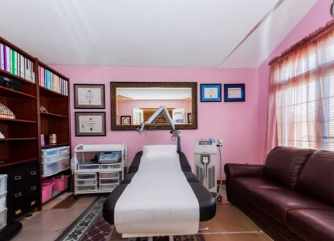 interior of a spa medical room with a large bed in the centre in front of a pink wall and bookshelves to the left