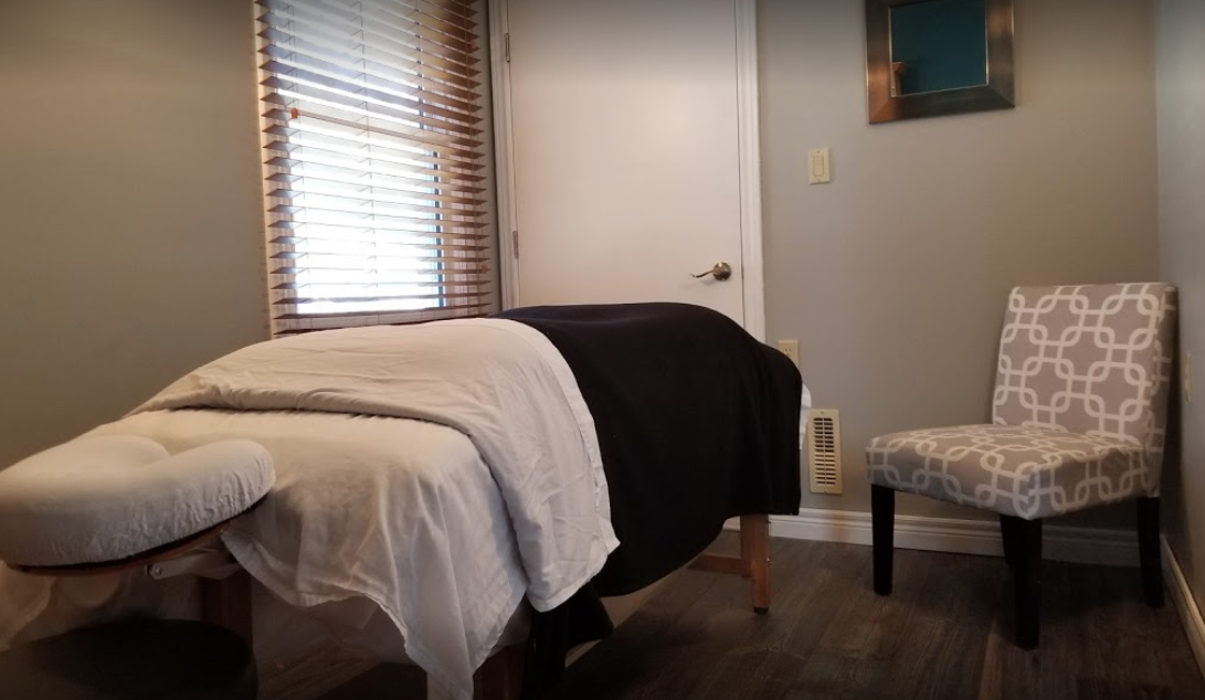 interior of a massage room with a made bed and a chair in the corner