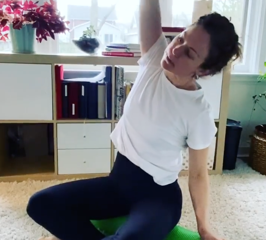 woman stretching at home on a foam roller with books and various office items behind her