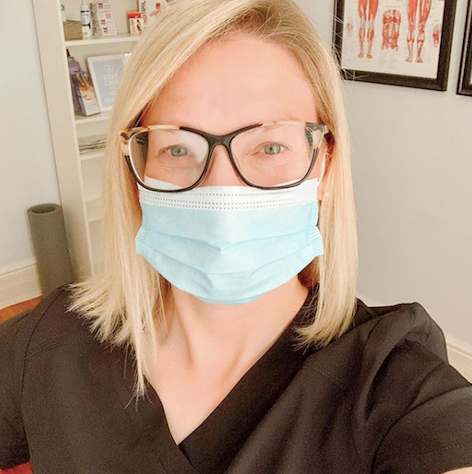woman wearing a mask, glasses and scrubs appearing to be smiling