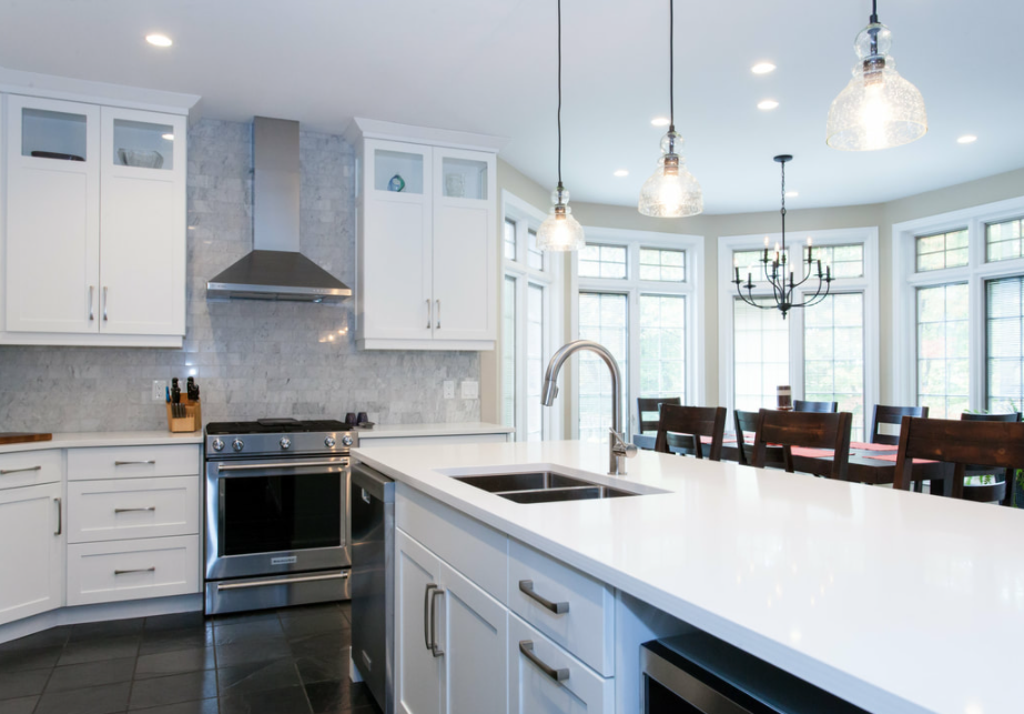 interior of a recently renovated kitchen with large island with white counters and cabinets and some stainless steel accents throughout