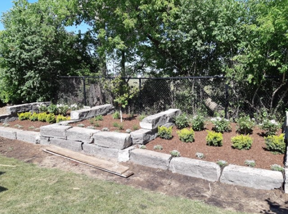 backyward being landscaped with large rocks creating different levels and shrubs in three rows going vertical