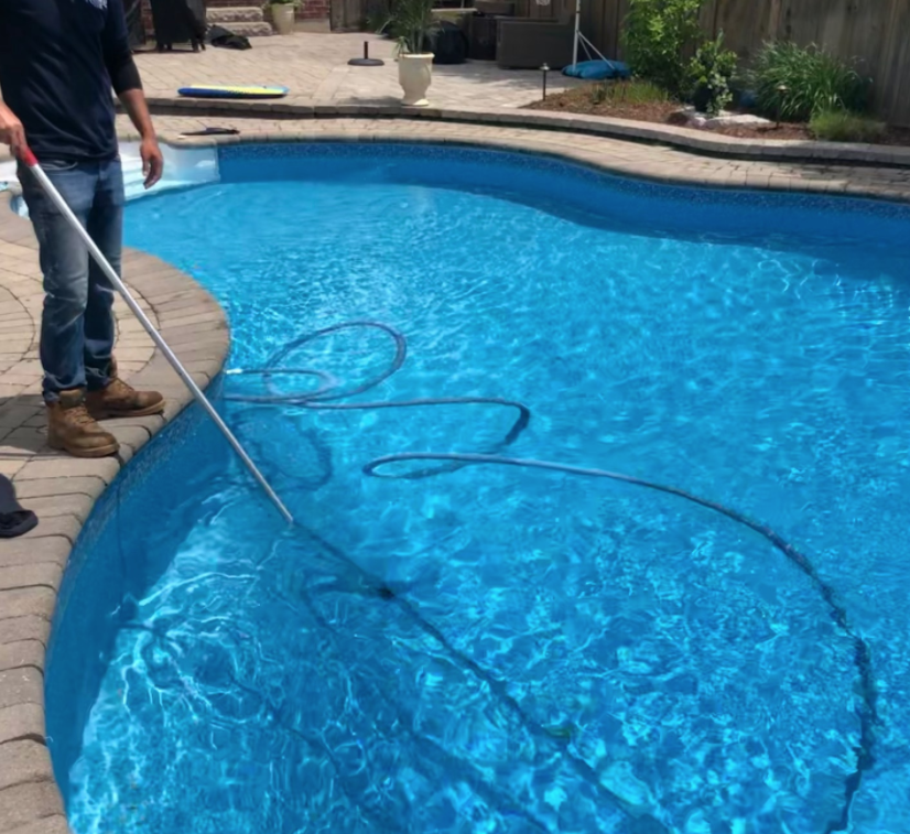 man holding a pool vacuum cleaning a pool on a sunny day