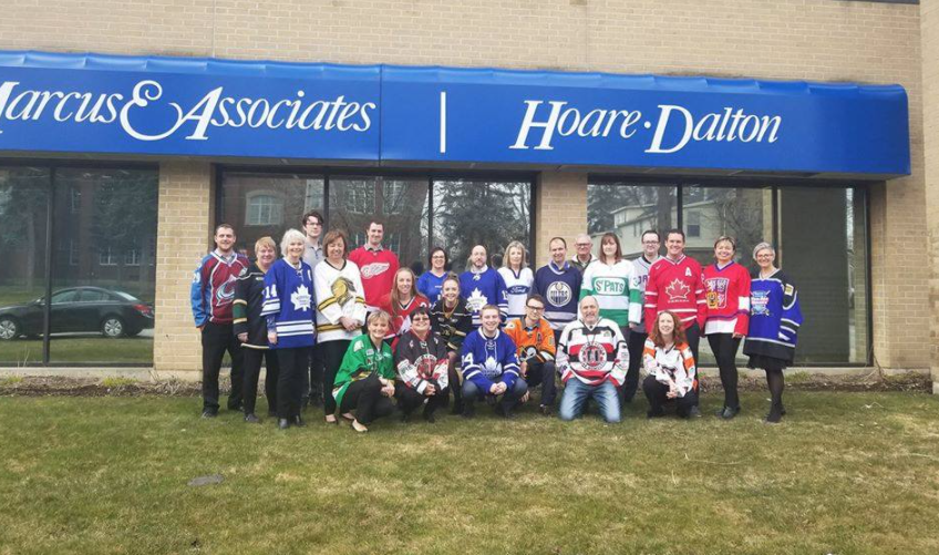 group of people standing outside an office building wearing hockey jerseys under a blue company banner
